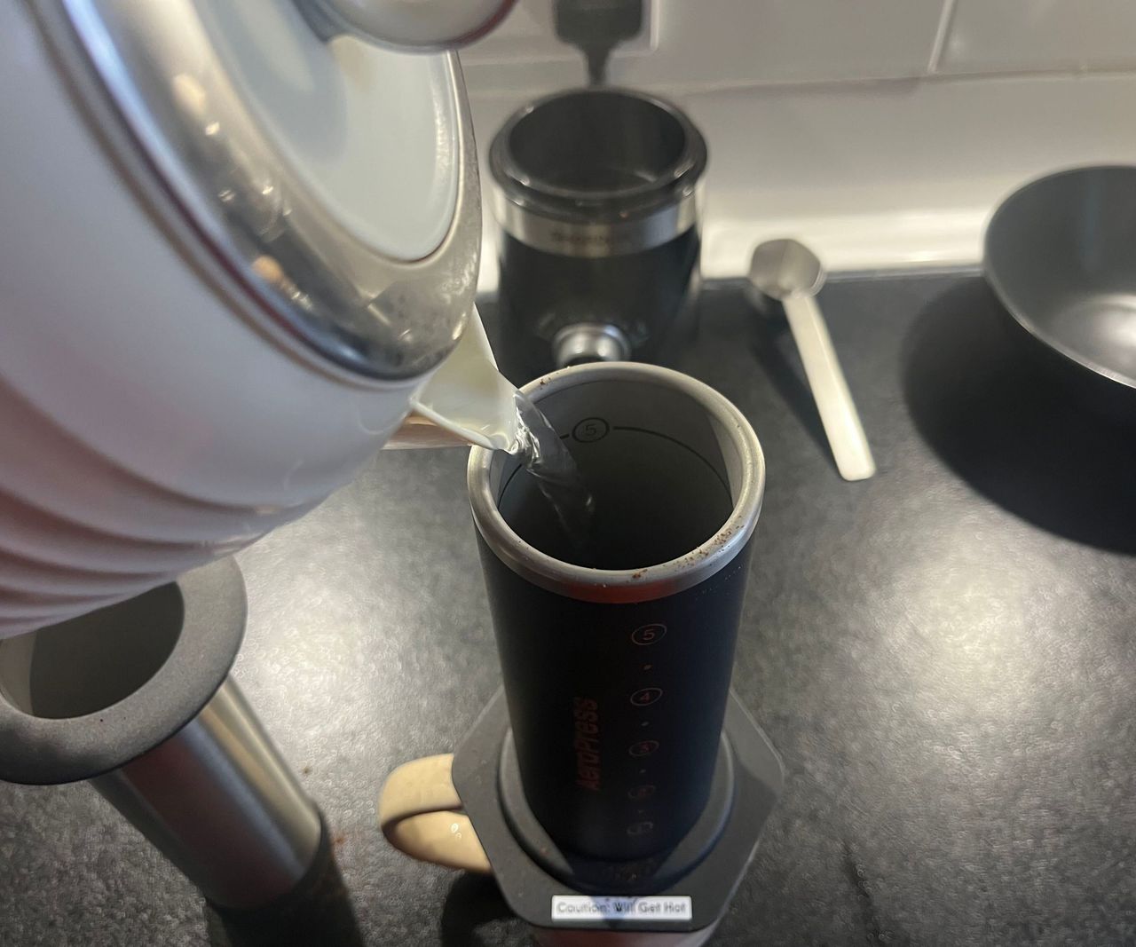 Pouring water from an electric kettle into a black AeroPress.
