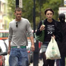Jamie Dornan and Keira Knightley walk along a street with shopping bags.