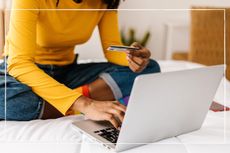 close up of woman sitting on her bed using credit card to shop online using a laptop