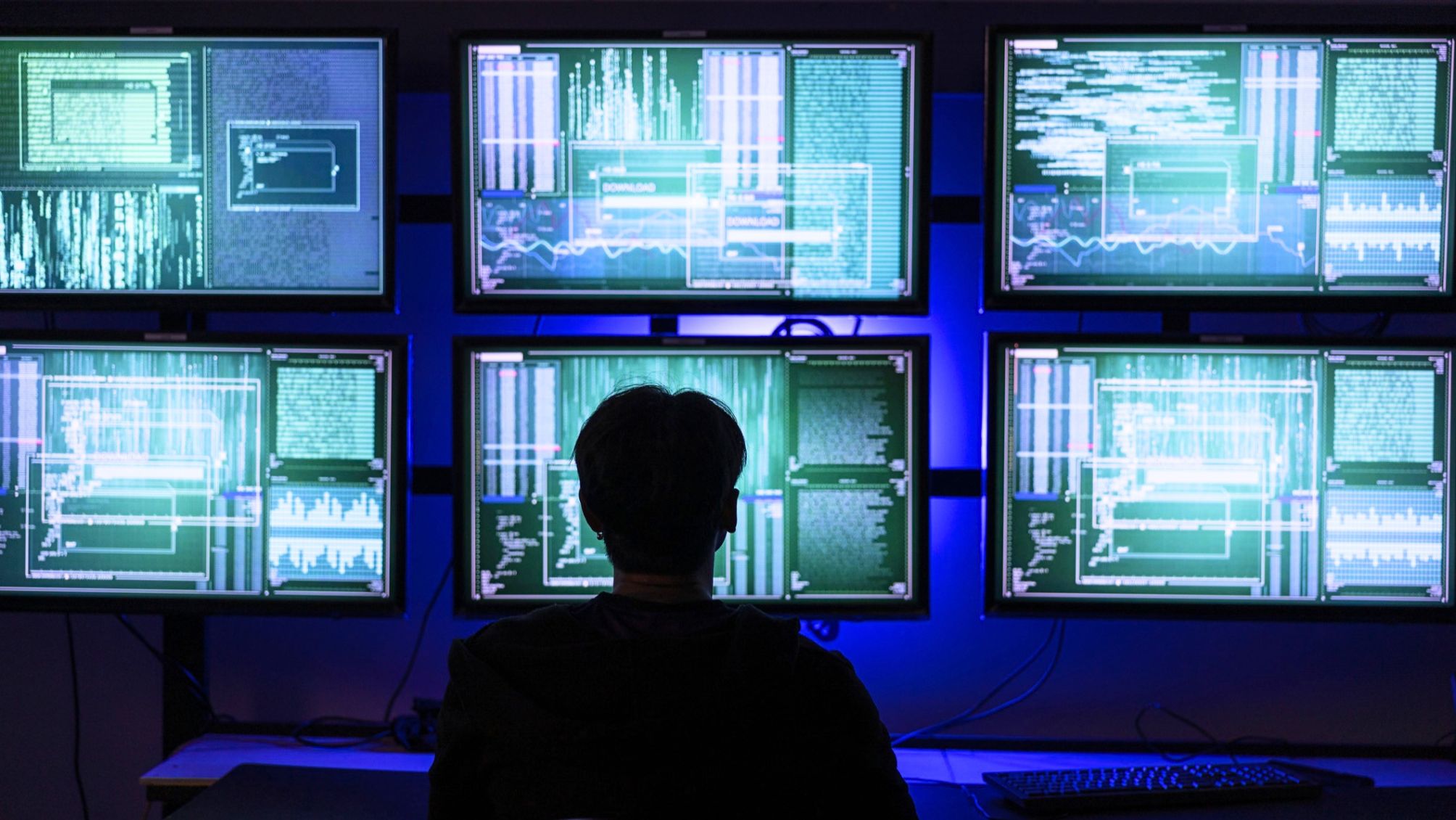 A hacker working on six different computer screens.