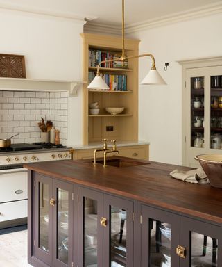 devol yellow kitchen with a dark brown island with brass accessories, hardware and tap
