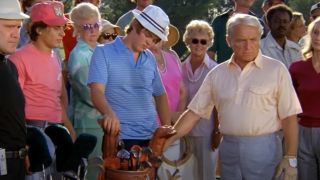 Ted Knight standing over his golf bag in front of a crowd of people.