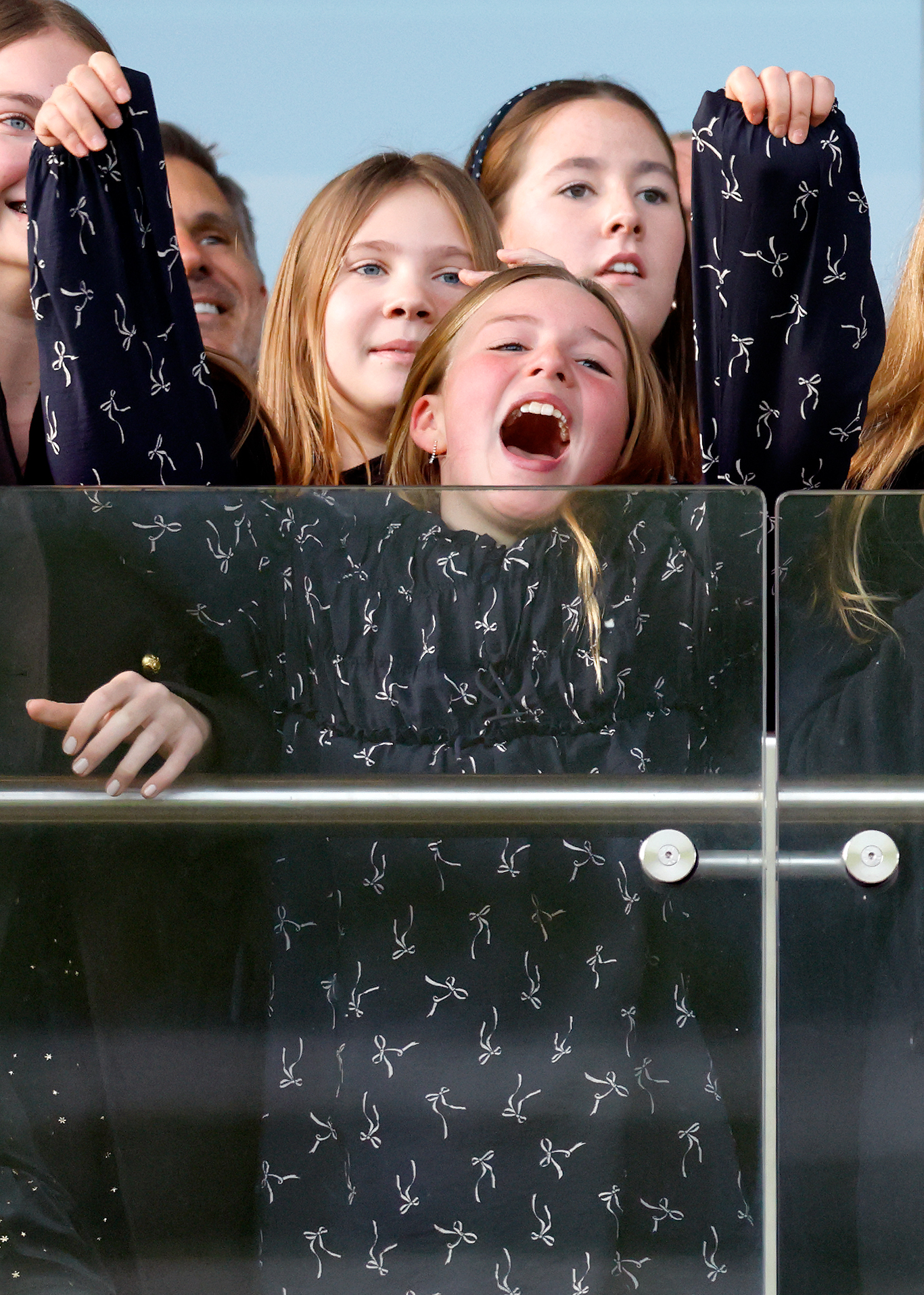 Mia Tindall wearing a blue dress and cheering behind a glass balcony