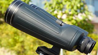 Side view of a large pair of binoculars with a rubber grip in a sunlit garden.