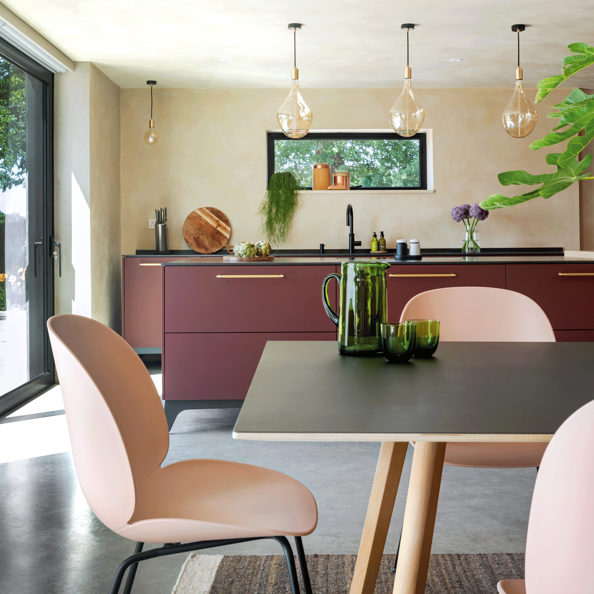 open plan kitchen dining area with a dining table and pink dining chairs and a budgundy kitchen island and matching cabinetry