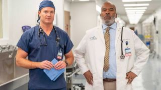 Dr Bruce (Josh Lawson ) stands besides a grumpy-looking Dr Ron (David Alan Grier) in a brightly-lit hall within St. Denis Medical Hospital in NBC's new comedy series.