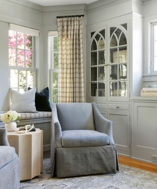 sitting room with light gray walls and built-in cabinetry, gray armchair and wooden side table