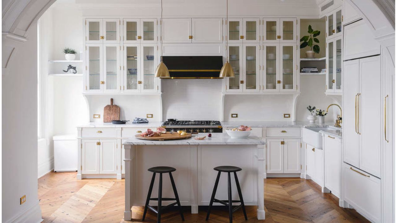 fitted white country kitchen through period archway with white kitchen island and brass fittings on parquet floor and white cabinets