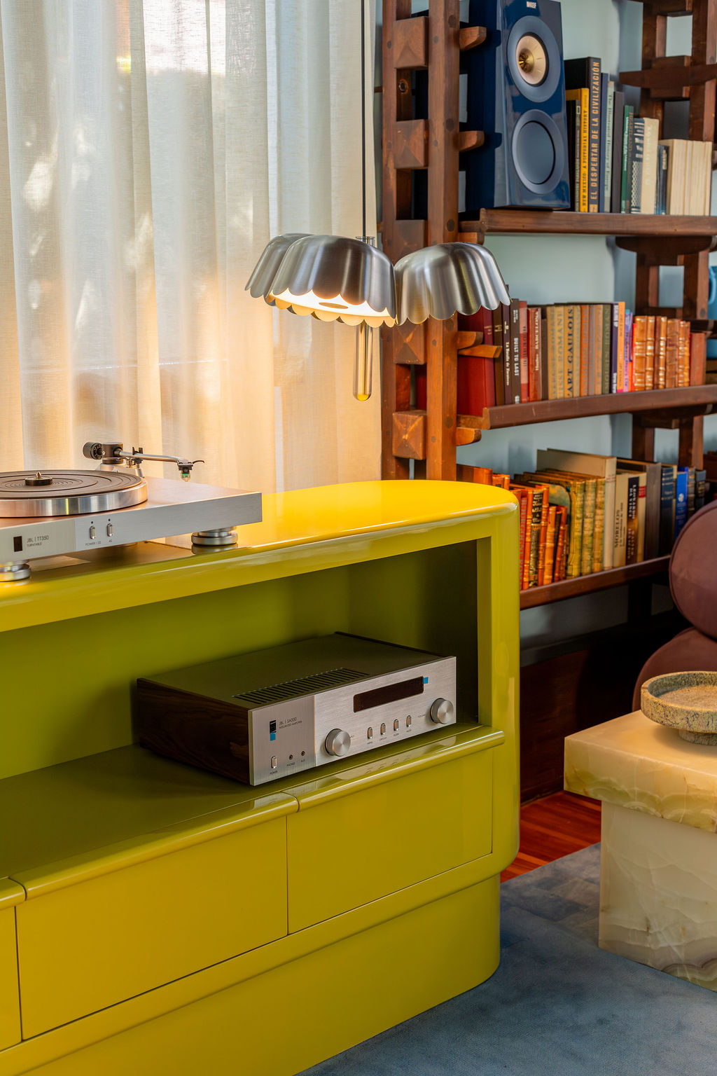 close up of a lime green credenza in a living room with a record player and speakers. sheer curtains and book-shelf in the background filled with books and speakers
