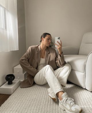 Woman sits on floor wearing beige blazer, white linen trousers and trainers