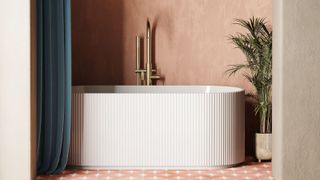 A modern freestanding bath with a fluted white exterior stands against a warm terracotta plaster wall. A gold floor-mounted tap is positioned beside the bath. The floor features patterned terracotta tiles with a white star design. A deep blue curtain hangs to the left, partially enclosing the space, while a potted green palm plant sits to the right in a gold-toned planter.