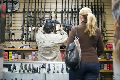 A gun sales person removes a rifle from the wall of a gun shop