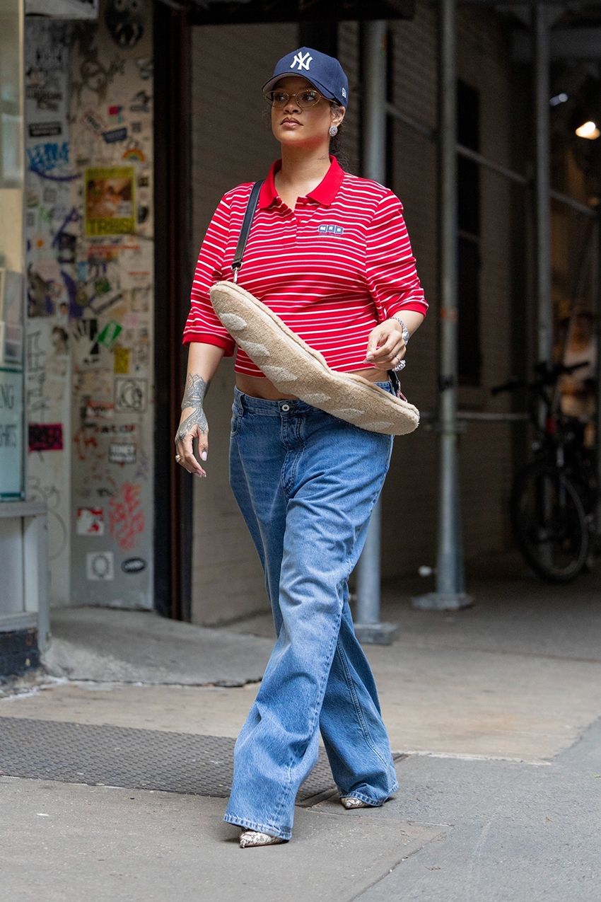 Rihanna wearing a red polo shirt, jeans, a baguette bag, and a NY Yankees baseball cap