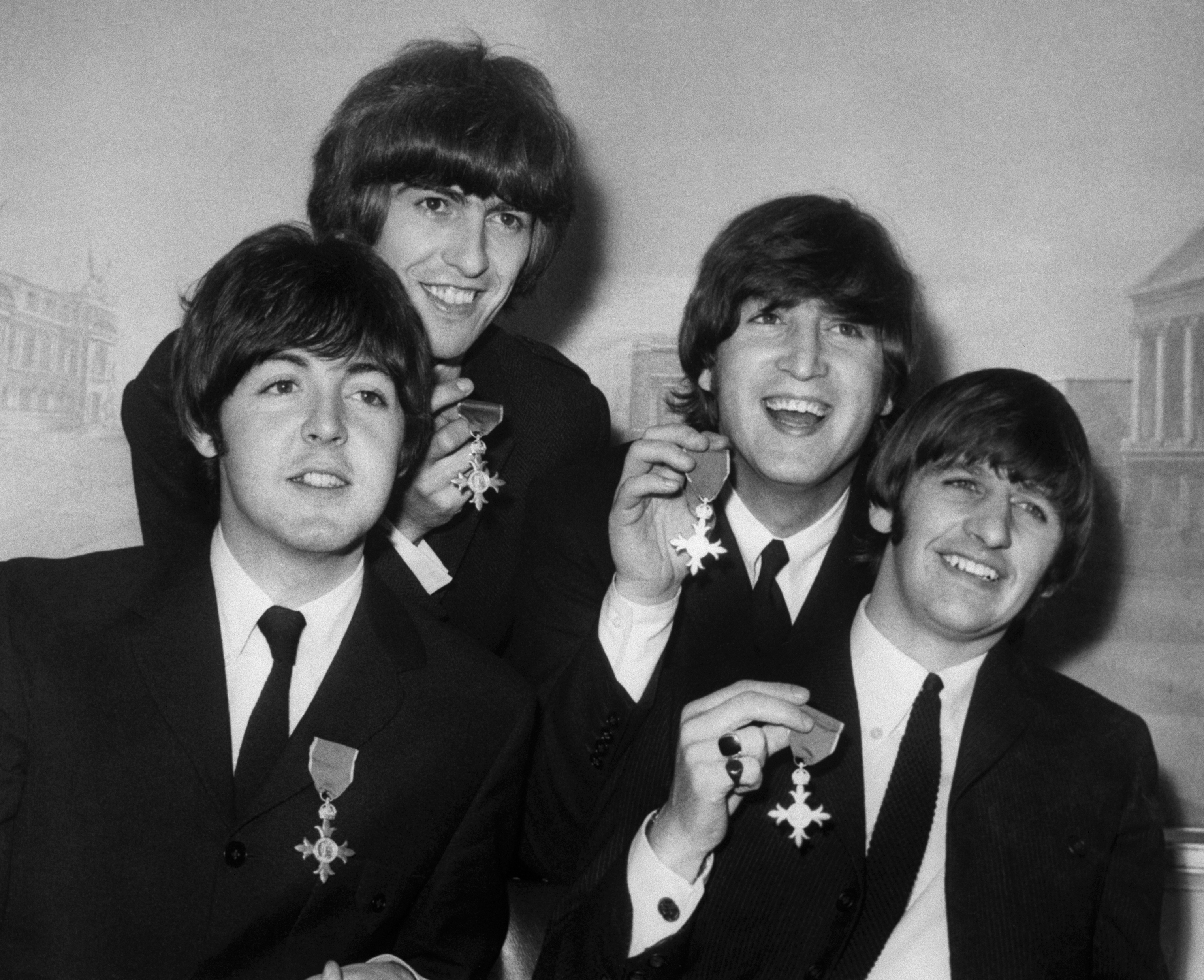 The Beatles wearing suits and holding up their MBE medals