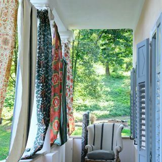 balcony with different fabrics hanging from top for privacy, blue shutters, upholstered armchair