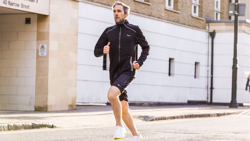 Man running along street wearing shorts and running jacket