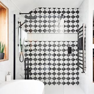 a shower enclosure clad in patterned black and white tiles and pale marble tiles,. with black shower fittings, chrome towel rail and a glass screen