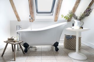 freestanding slipper bath and rustic wooden stool in in room with white walls with beams
