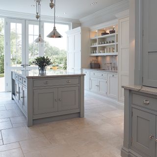 A shaker style kitchen with a large gray island below two pendant ceiling lights