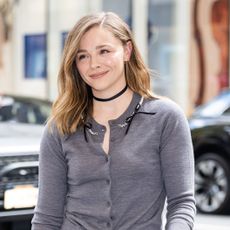 Chloe Grace Mortez wearing a gray cardigan, black fringe skirt, and black thigh high boots