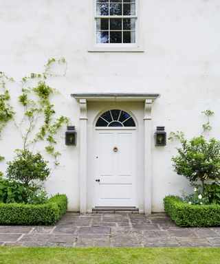 An example of very small front garden ideas with climbing plants up a white house beside the front door, with gray patio.