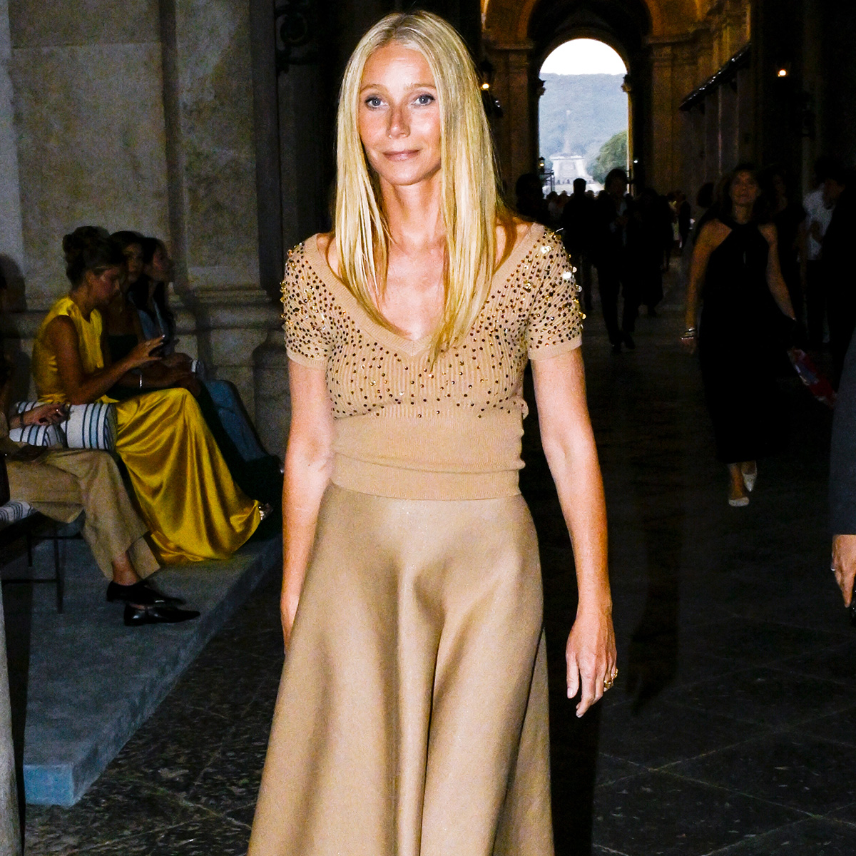 Gwyneth paltrow wears a tan top, tan skirt, and brown pumps.