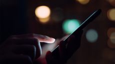 Mobile app security concept image showing a person's hand illuminated by a smartphone screen on a dark street.