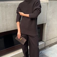 Woman wears a chocolate brown ribbed Toteme sweater with Cos trousers and white Manolo Blahnik Maysale slingbacks. 