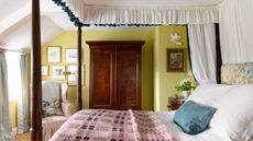 Bedroom with citron green painted walls, a mahogany four-poster bed with a canopy, a floral headboard and a pink Welsh blanket, and a large mahogany wardrobe beside a pale pink armchair.