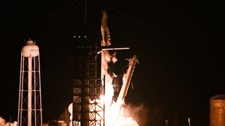 a white rocket lifts off at night above a plume of fire and smoke