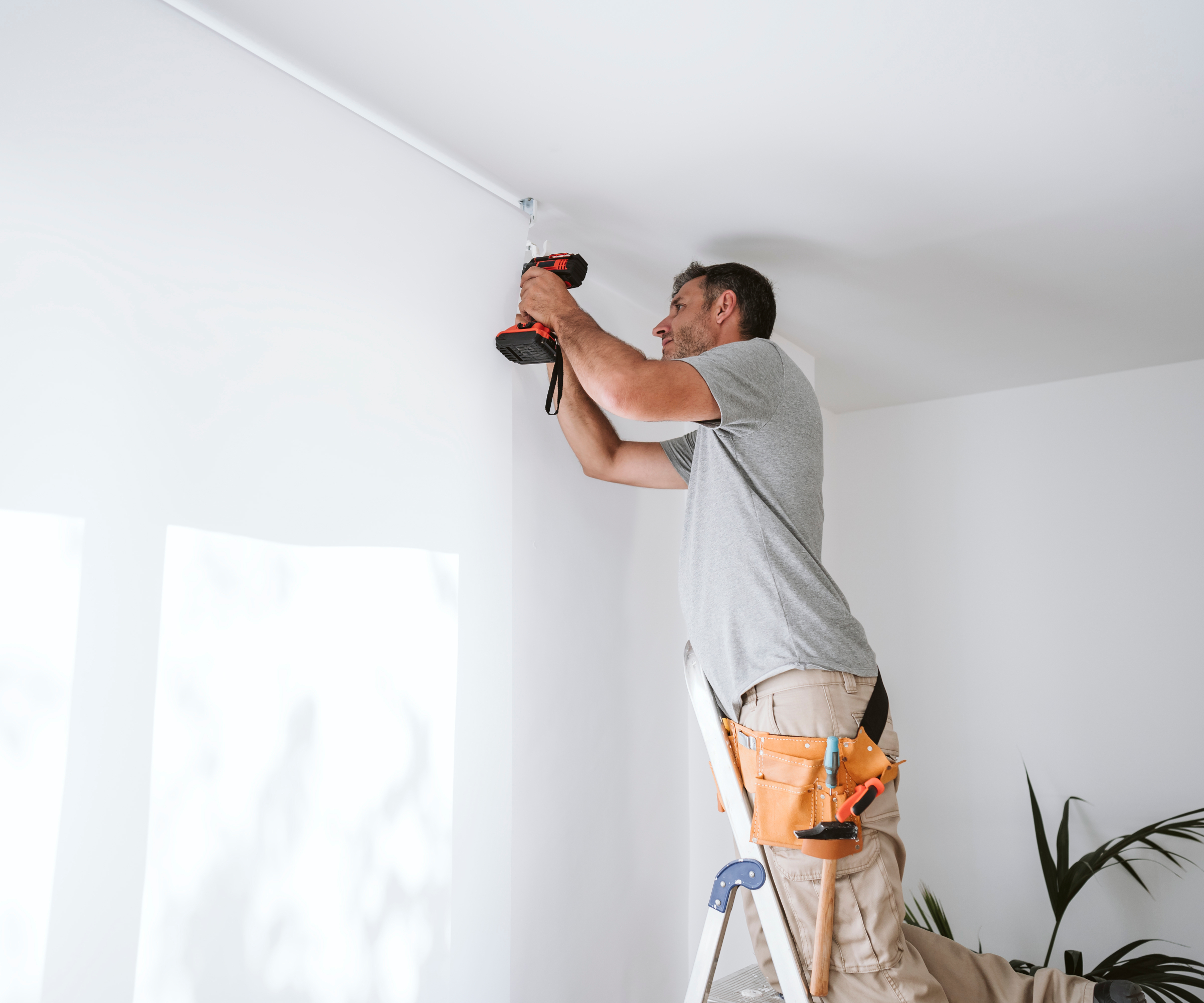 man on ladder drilling hole for curtain pole above window