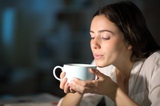Woman blowing to cool hot coffee in the night at home.