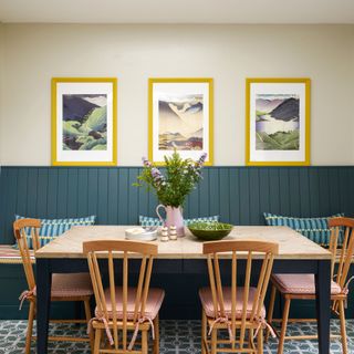 gallery wall yellow framed artwork on cream wall behind dark blue panelling banquette seating area which is paired with table and farmhouse chairs