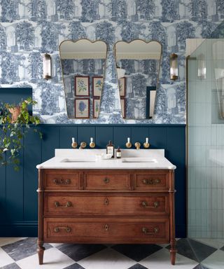 bathroom with blue and white illustrated wallpaper, dark blue wall panelling, dark wooden vanity and traditional details