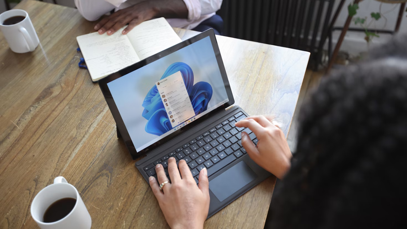 A woman at a table using a Windows laptop, opposite sits a man, neither show their face