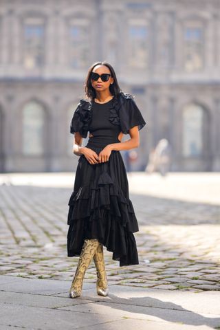 PARIS, FRANCE - MARCH 19: Emilie Joseph @in_fashionwetrust wears black sunglasses, a black ruffled puffy short sleeves / cut-out waist / asymmetric midi dress from Magalie Pascal, beige and black shiny leather snake print pattern pointed / heels knees boots / high boots from Paris Texas,, during a street style fashion photo session, on March 19, 2022 in Paris, France. (Photo by Edward Berthelot/Getty Images)