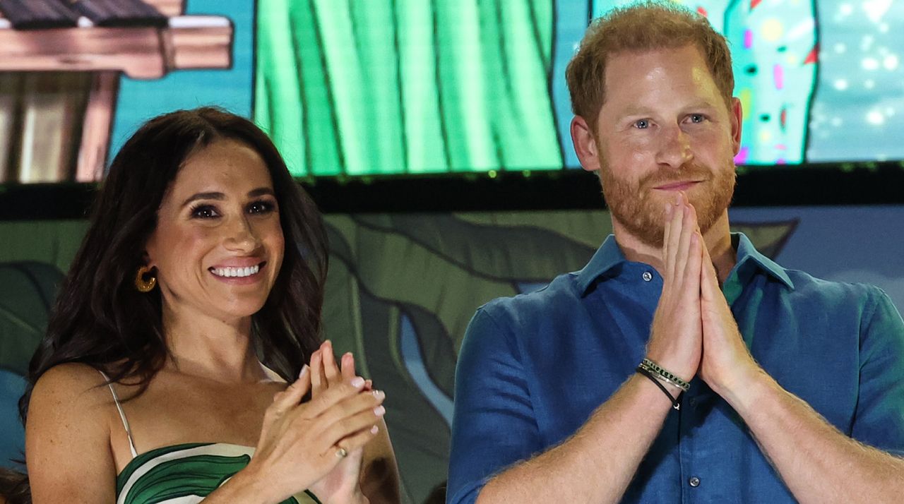 Meghan Markle wears a green and white leaf-print dress, and applauds next to husband Prince Harry