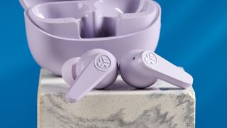 the jlab go pods anc earbuds in lilac with a lilac charging case and built in usb-c cable against a blue background on a marble stand