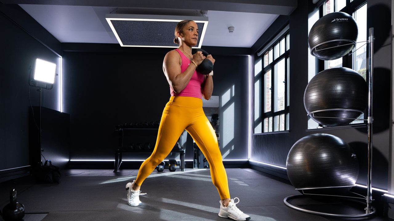 Trainer Joslyn Thompson Rule stands in a split stance holding a kettlebell at her chest.