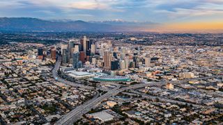 A wide angle photo of downtown Los Angeles showing a sunset and snowy mountains in the background