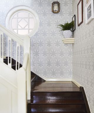 A hallway wallpaper idea with dark wooden stairs, white baulstrade and white and blue wallpaper