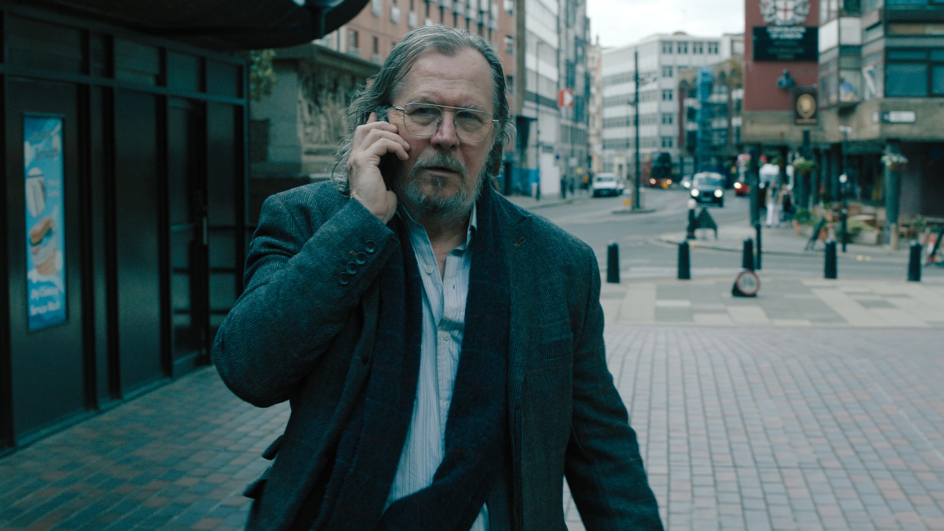 Gary Oldman camina por la calle hablando por teléfono en Slow Horses