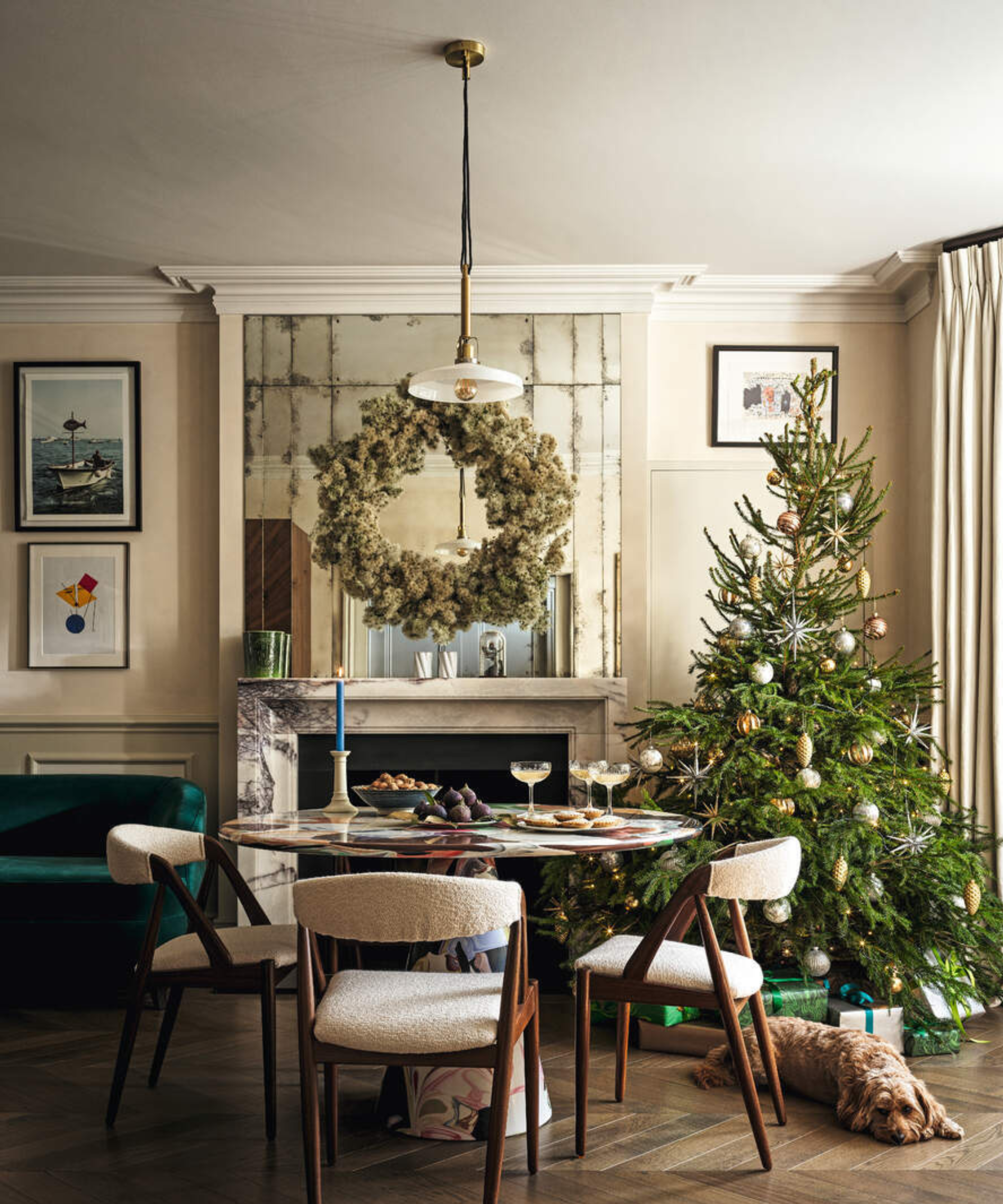 a dining room with a round dining table and three dining chairs, a Christmas tree, and a fireplace with a large wreath above it