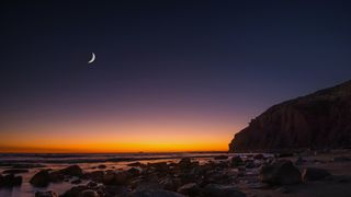 Thin crescent moon rising above a beach at sunset. 