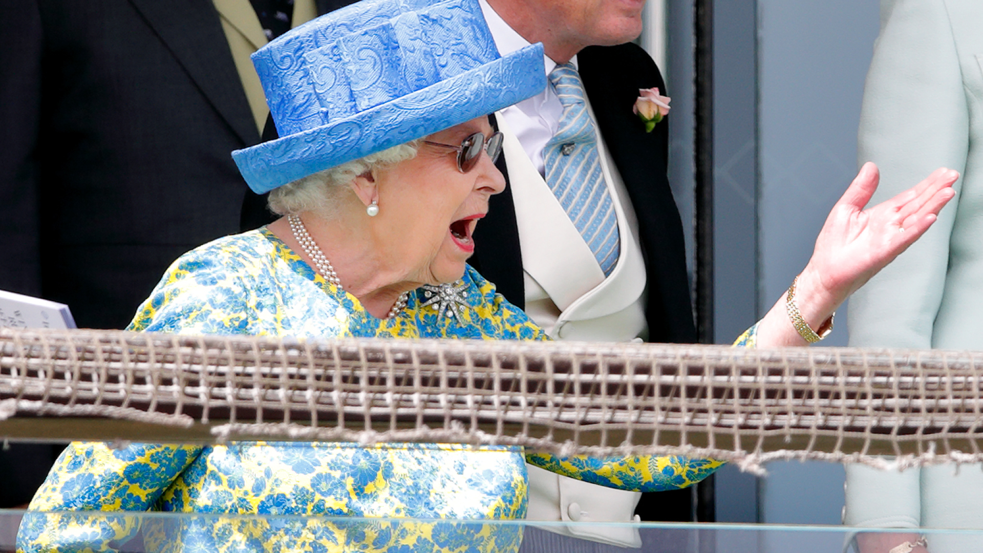 Queen Elizabeth reacting a blue hat and floral dress shouting