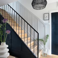 A hallway with a staircase with black railing and grey wall panelling in a wainscoting style