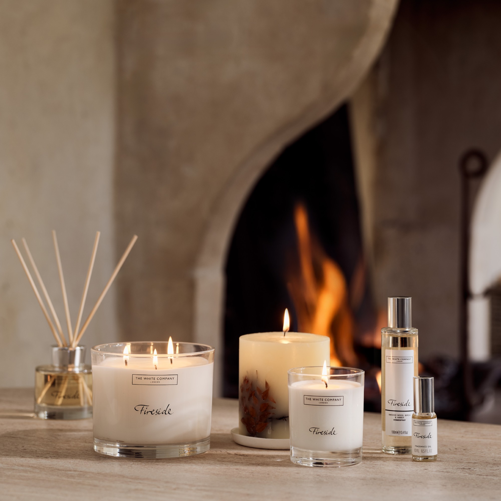 The White Company's Fireside home fragrance range with a lit fireplace in the background