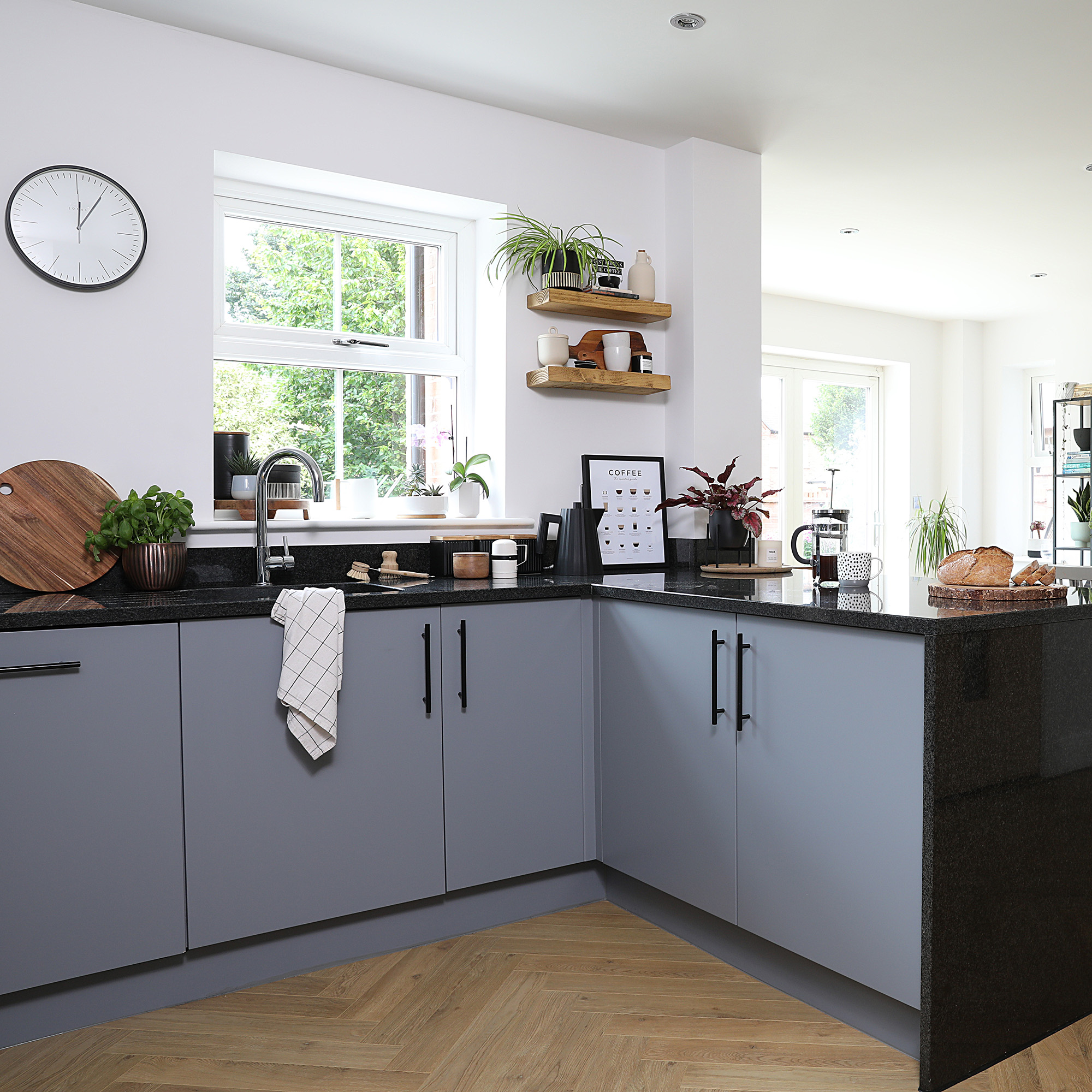 open plan L-shaped kitchen with white walls and grey painted cabinetry and black bar handles and topped with black waterfall worktops