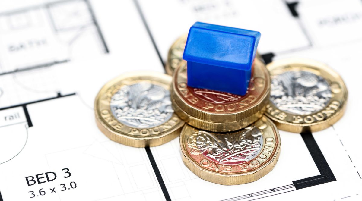 Small plastic house sitting on top of floorplans and pound coins