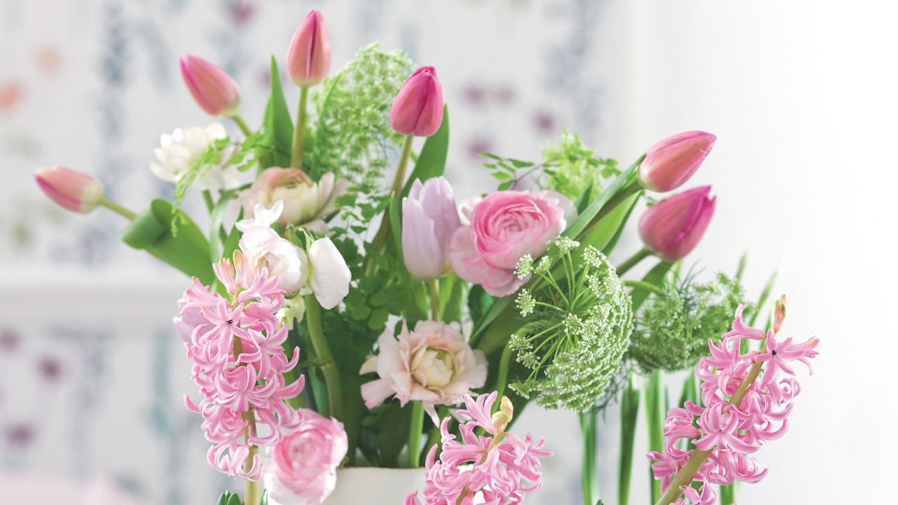 Cut flowers in white vase including pink tulips, roses and pink hyacinth